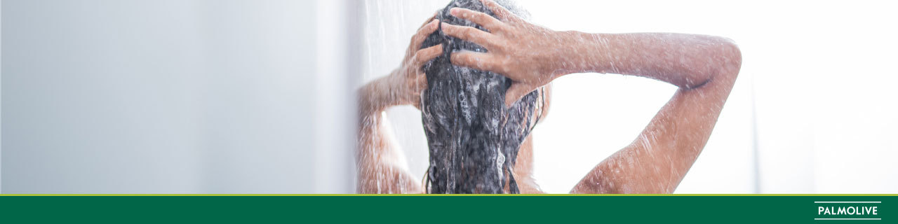 Pessoa de costas no chuveiro lavando o cabelo com um shampoo para cabelos oleosos.