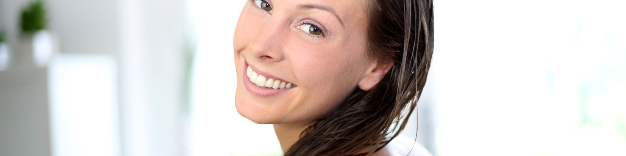 Mulher sorridente com cabelos úmidos após aplicar condicionador anticaspa no comprimento dos fios.
