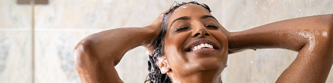 Mulher tomando um banho de chuveiro, lavando o cabelo com um shampoo anticaspa