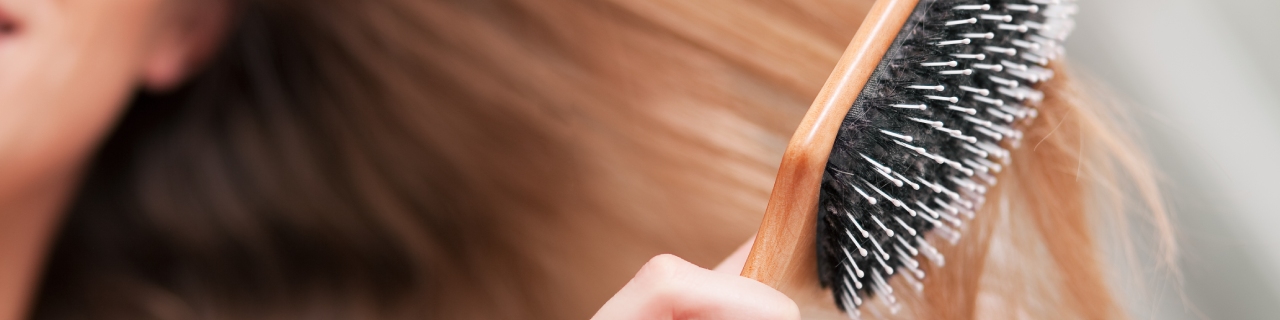 Uma mulher penteando o cabelo, observando atentamente a saúde dos fios para entender como saber se seu cabelo está danificado