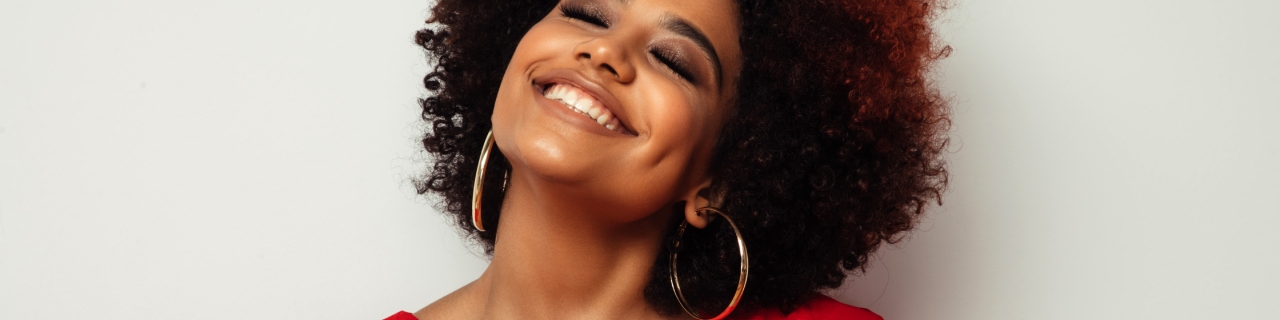 Mulher com cabelos cacheados, sorrindo de felicidade, pois seus fios estão hidratados e macios após o uso correto do shampoo e condicionador para cachos.  